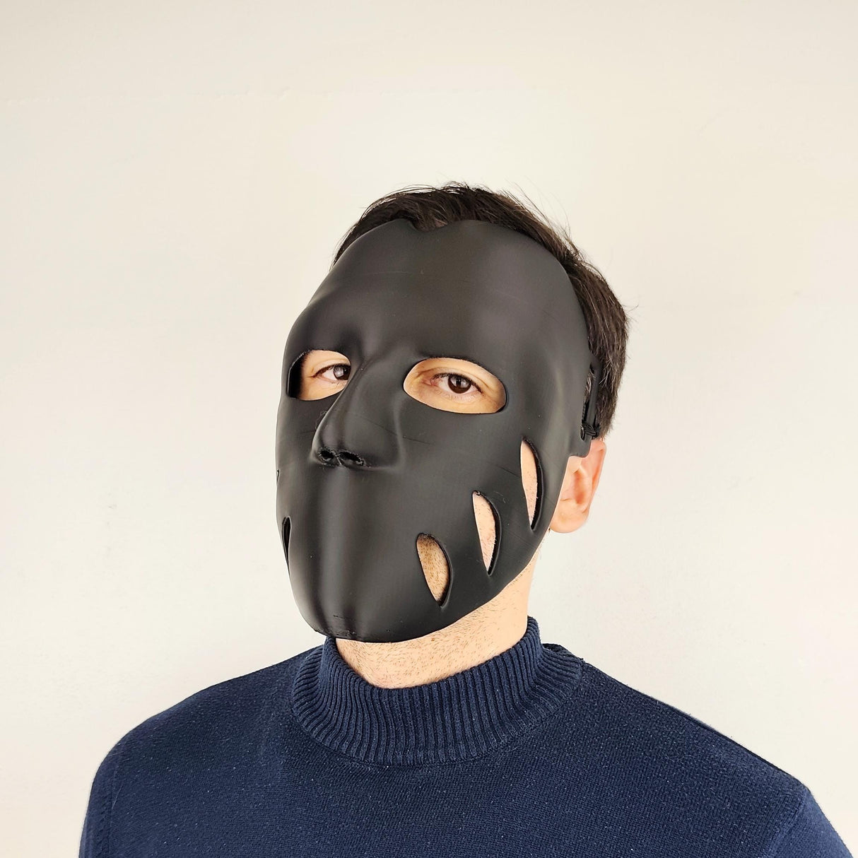 Person wearing a matte black 3D printed face mask with organic cutouts and a sleek, form-fitting shape, secured with adjustable elastic straps.