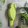 3D printed wall decor shaped like a minimalist parrot silhouette in a bold green color, matte PLA design mounted on a textured interior wall with plants nearby