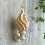 3D printed wall decor shaped like a stylized torch flame, minimalist matte PLA sculpture mounted on a textured neutral wall with greenery nearby