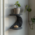 3D printed double-tier spiral wall shelf in matte dark PLA, with a twisting ribbed support between two round shelves, styled with small decor in a modern interior.