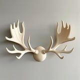 3D printed wall decor shaped like stylized cream-colored moose antlers in three pieces (two antlers and a round base) mounted on a smooth light wall.