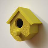 3D printed birdhouse with round entrance and cylindrical perch made of matte PLA plastic, mounted on a wall casting a long shadow in natural light.