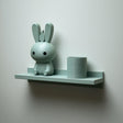 3D printed wall shelf with a slim back-edged ledge holding a rounded bunny character and a cylinder pot, mounted on a light-colored wall.