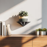 3D printed pyramid-shaped wall shelf in black, holding a small plant pot, displayed above a wooden cabinet as modern geometric wall decor