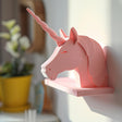3D printed wall shelf shaped like a minimalist pastel unicorn head with a twisted horn, matte PLA surface, used as a small floating ledge in a bright room.
