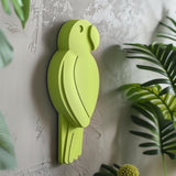 3D printed wall decor shaped like a minimalist parrot silhouette in a bold green color, matte PLA design mounted on a textured interior wall with plants nearby