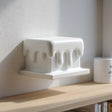 3D printed wall shelf shaped like a rectangular block with smooth dripping edges made of matte PLA plastic, mounted above a wooden shelf in soft natural daylight.