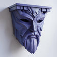 3D printed matte PLA wall shelf with an angular fantasy guardian mask face supporting a small display ledge on a light wall.