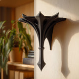 Small gothic-style 3D printed wall shelf bracket with a pointed spire shape, mounted on a light wall and used as a decorative display ledge.