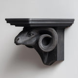 3D printed ram head wall shelf with curved horns supporting a flat floating ledge, mounted on a clean minimalist wall.