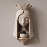 3D printed wall mounted fairy face planter shelf with a small succulent pot, featuring a serene sculptural face and crown-like details, displayed on a neutral wall.