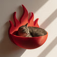 3D printed wall mounted cat shelf bed shaped like stylized flames, holding a resting cat in warm natural sunlight near a window.