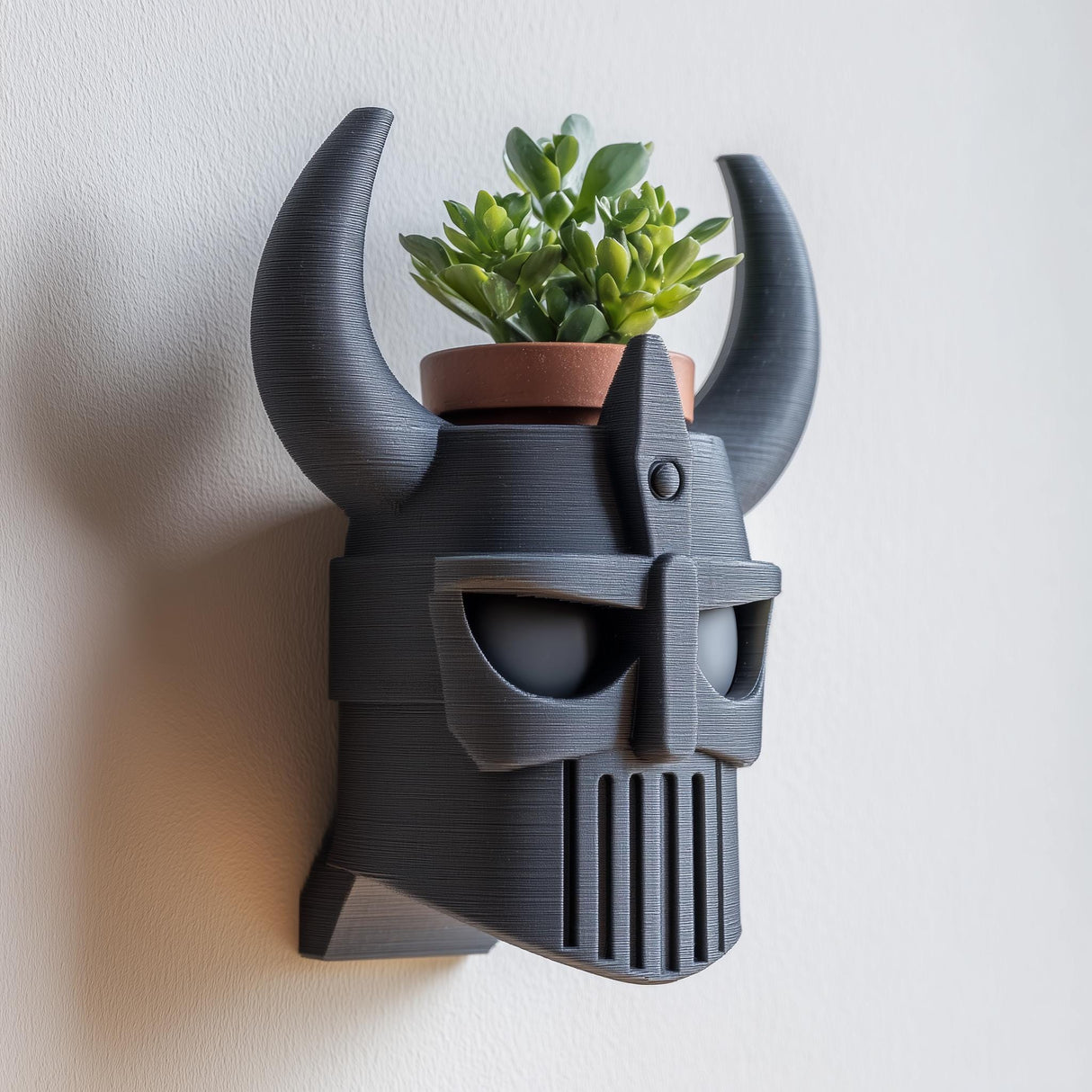 3D printed wall mounted Viking helmet planter shelf in matte dark PLA with horned helmet design and small plant pot, displayed on a minimalist interior wall.
