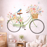A watercolor illustration of a vintage mint-green bicycle on a white background. A wicker basket on the front is filled with pink and yellow roses, and a similar arrangement sits over the back wheel. A small bluebird is perched on the brown seat, and two light-blue butterflies float nearby.
