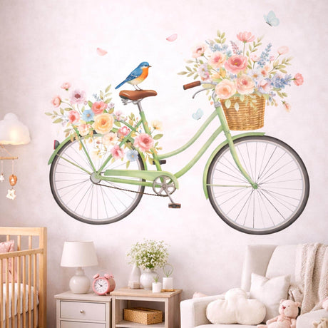 A watercolor illustration of a vintage mint-green bicycle on a white background. A wicker basket on the front is filled with pink and yellow roses, and a similar arrangement sits over the back wheel. A small bluebird is perched on the brown seat, and two light-blue butterflies float nearby.