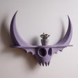 3D printed dark fantasy skull wall shelf with curved horns and sculptural gothic form, mounted on a light neutral interior wall.