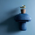 3D printed modern mushroom wall shelf with rounded dome cap and smooth sculptural base, mounted on a blue minimalist interior wall.