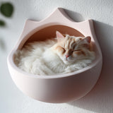 3D printed crown-shaped wall mounted cat bed in matte blush PLA with a fluffy cream cat sleeping inside, installed on a textured light wall.