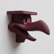 3D printed dark surreal creature wall shelf with elongated beak-like sculptural form and integrated top shelf, mounted on a light interior wall.