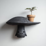 3D printed cute mushroom character wall shelf with smiling face and wide cap surface, mounted on a clean modern interior wall.
