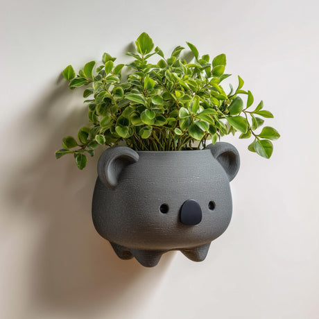3D printed koala-shaped wall planter pot in matte dark gray PLA, mounted on a neutral wall and holding a small green houseplant.