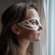 3D printed minimalist contour eye mask with flowing side cutout panels, worn in side profile near a window with soft daylight, visible print texture.