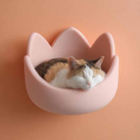 3D printed kawaii crown-shaped wall mounted cat bed in matte blush PLA with a calico cat sleeping inside against a warm peach wall.