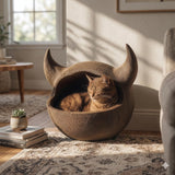Horned floor cat cave bed with a rounded enclosed pod shape and two curved horn accents, textured surface, with a cat resting inside in a cozy living room.