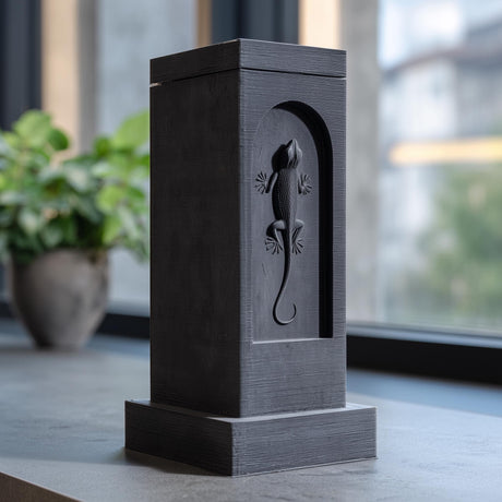 3D printed architectural pet ashes urn tower with an arched recessed niche and raised gecko relief on the front, displayed on a tabletop near a window.