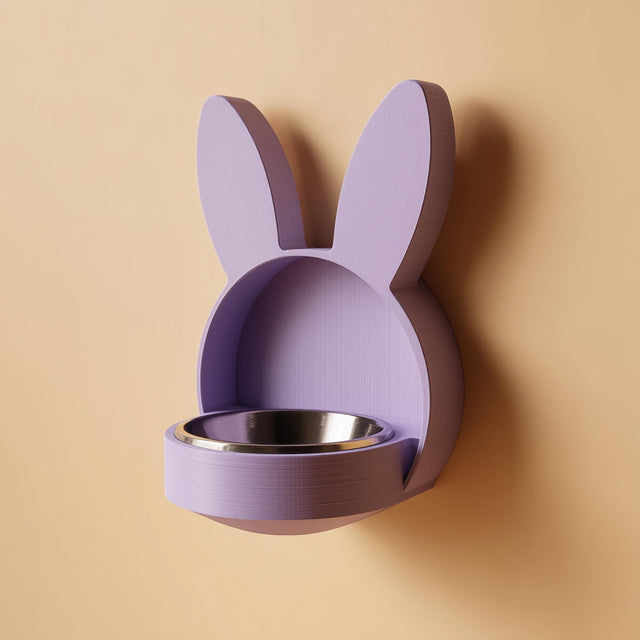 3D printed bunny-shaped wall mounted pet bowl holder with long ears and a round bowl opening, shown on a plain wall with a bowl placed inside.