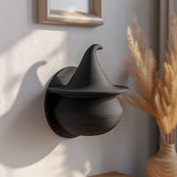 3D printed witch hat wall decor shelf in matte PLA mounted on a soft neutral wall with warm natural lighting and dried plants nearby.