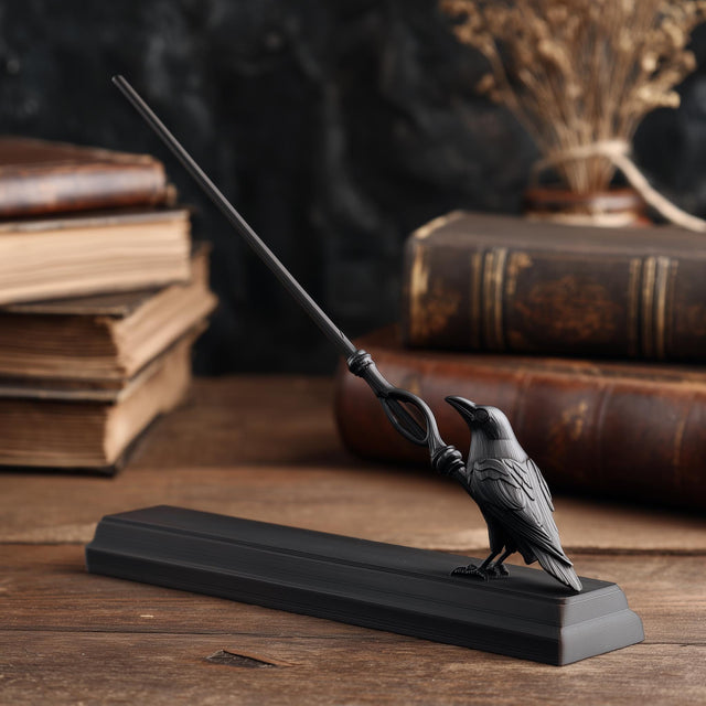 3D printed raven magic wand with matching display stand in matte PLA displayed on a wooden desk with vintage books and gothic decor.