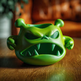 Monster-shaped jewelry organizer bowl with an angry face, pointed teeth, and small side arms on a wooden table in warm indoor light.
