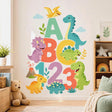 Colorful children’s illustration with large ABC letters and 123 numbers surrounded by friendly dinosaurs, a flying pterosaur, volcano, clouds, leaves, and plants on a white background.
