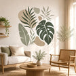 Abstract tropical botanical design on a white background with a large dark green monstera leaf, a sage banana-style leaf, slender leafy branches, and soft beige and tan organic shapes.