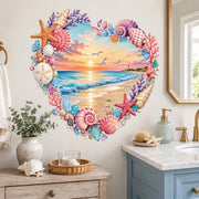 Heart-shaped watercolor beach scene with a pastel ocean sunset, gentle waves, flying seagulls, and a distant lighthouse, surrounded by pink, peach, cream, and lavender seashells, starfish, coral branches, sea glass, and small coastal stones.