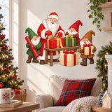 Santa and three smiling gnomes holding and wrapping red, green and gold Christmas gifts around a small wooden table.
