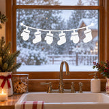 White vinyl window garland with six hanging Christmas stocking silhouettes on a gently curved line above a kitchen sink.