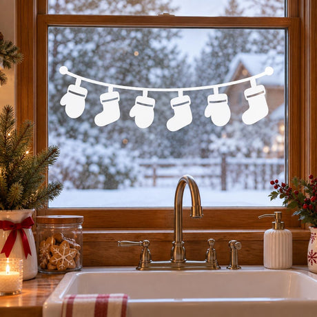 White vinyl window garland with six hanging Christmas stocking silhouettes on a gently curved line above a kitchen sink.