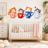 Four watercolor kittens sitting in striped, heart and daisy-patterned teacups as wall decals above a white nursery crib.