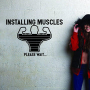 A motivational wall decal featuring a graphic of flexing muscles with the text 'INSTALLING MUSCLES PLEASE WAIT...' for gym.
