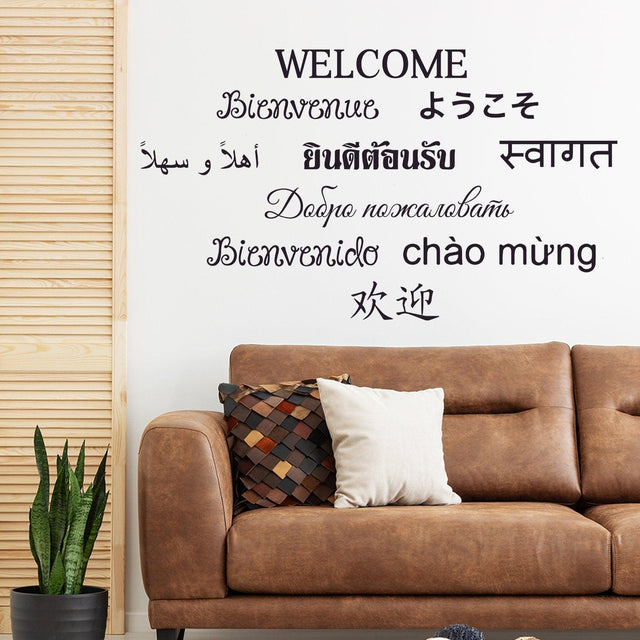 Decorative wall with multilingual 'Welcome' wall sticker above a modern couch.